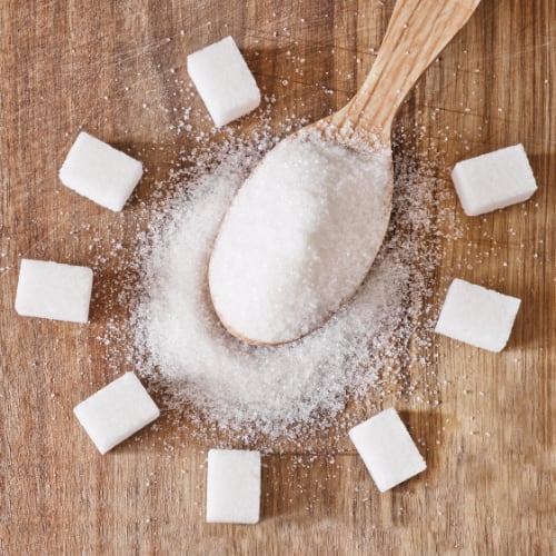 wooden spoon full of sugar with block sugar cubes around it on a wooden table