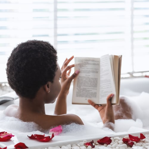 black woman relaxing reading a book in her bathtub