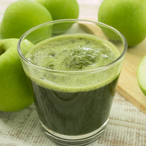 green apple juice on wooden cutting board with cut apples