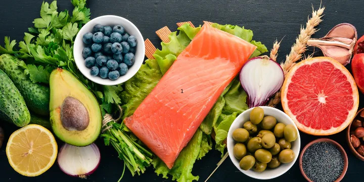 Assortment of whole foods including salmon, vegetables, berries, grains, olives, and nuts arranged in natural light