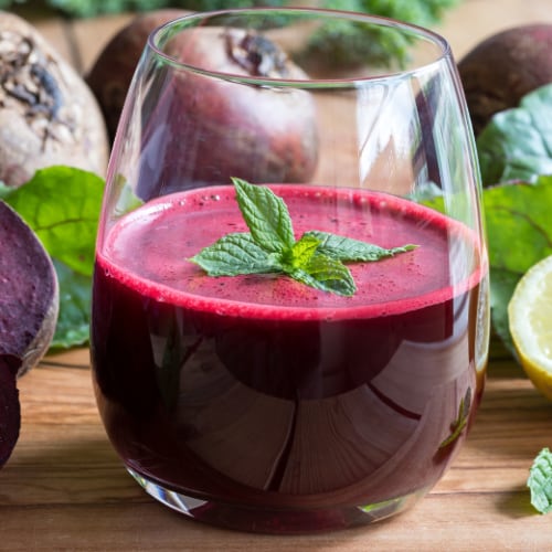red beet juice in glass on a wooden background with lemon and beets