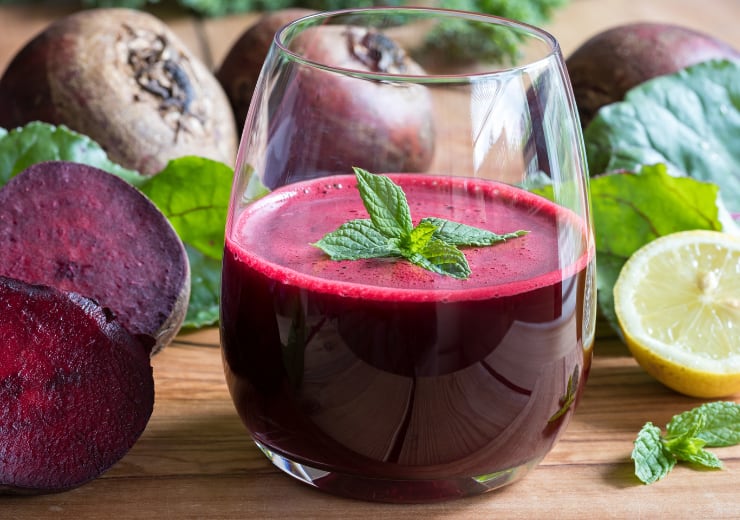 red beet juice in glass on a wooden background with lemon and beets