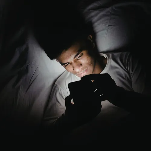 A person surrounded by screens and notifications late at night, reflecting continuous stimulation and limited downtime.