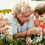 Elderly Woman Teaching Grandchildren About Flowers In A Field