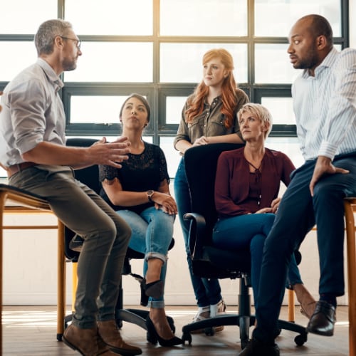 employees in an informal work meeting listening to a co-worker