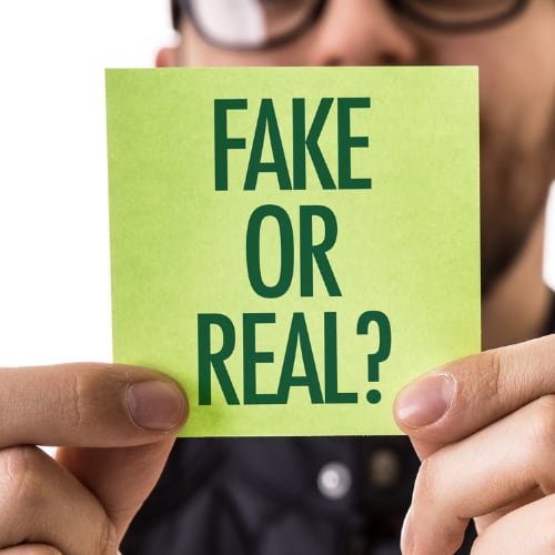 a man holding up a sign that says Fake or Real?