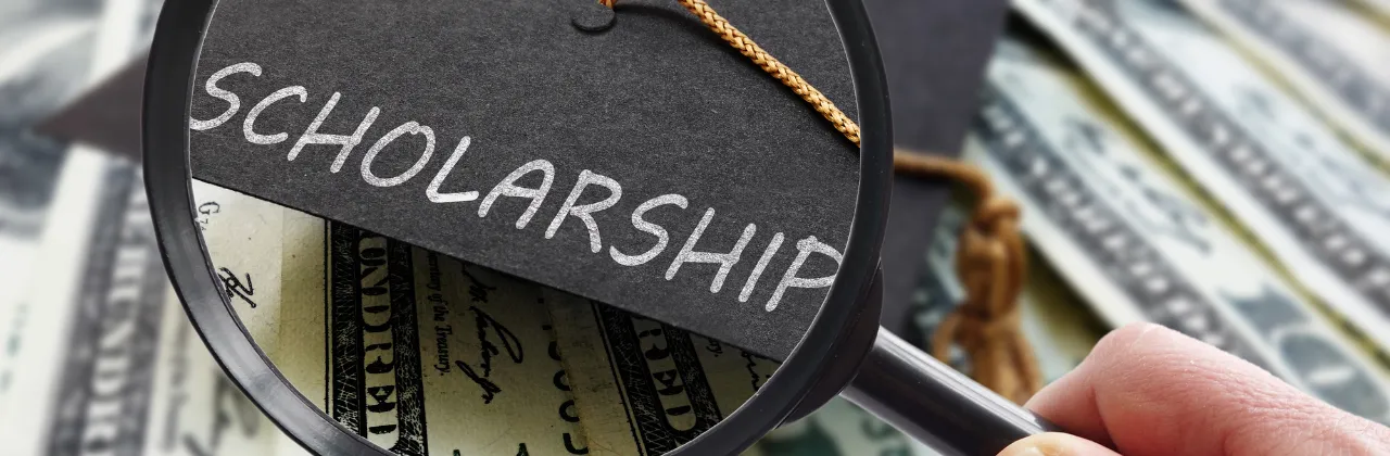 A magnifying glass reading the word 'scholarship' with a student graduation cap and money in the background.