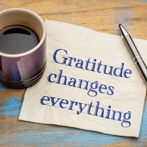 gratitude changes everything written on a napkin next to a coffee cup and pen