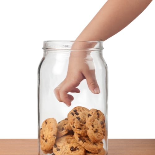 hand reaching into a glass jar of chocolate chip cookies