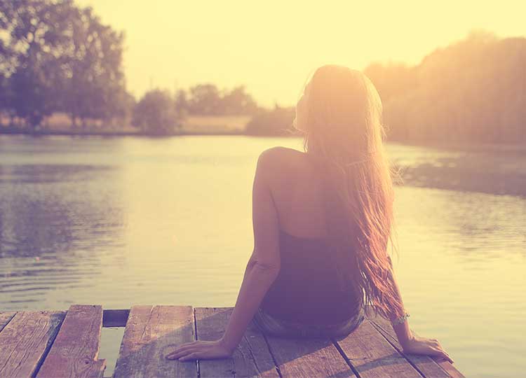 Happy Young Woman Sitting on Dock at Sunset