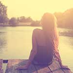 Happy Young Woman Sitting on Dock at Sunset