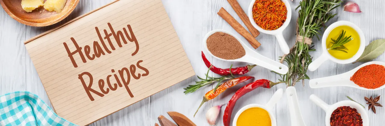 Notepad labeled 'Healthy Recipes' surrounded by whole-food ingredients, wooden utensils, and measuring cups on a white oak table.