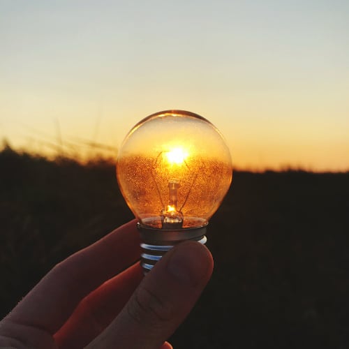 lightbulb held up to a sunset depicting fading energy