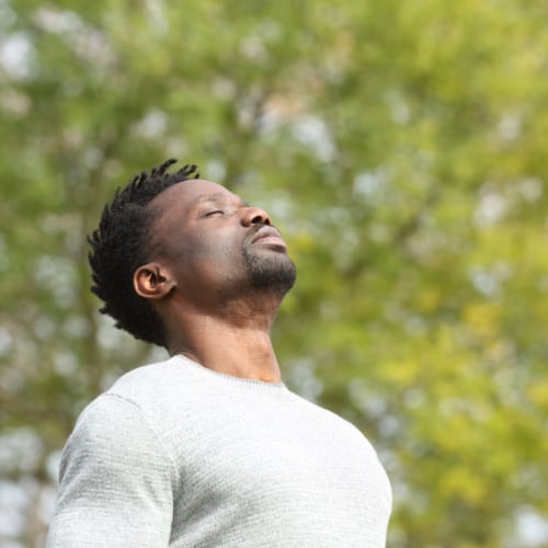 a man outside in a natural setting taking deep breaths 