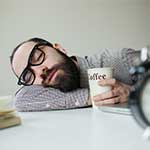 Bearded Man Sleeping at Desk with Coffee At 9 AM