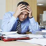 Stressed, Middle-aged man sitting at His Desk with a large stack of papers.