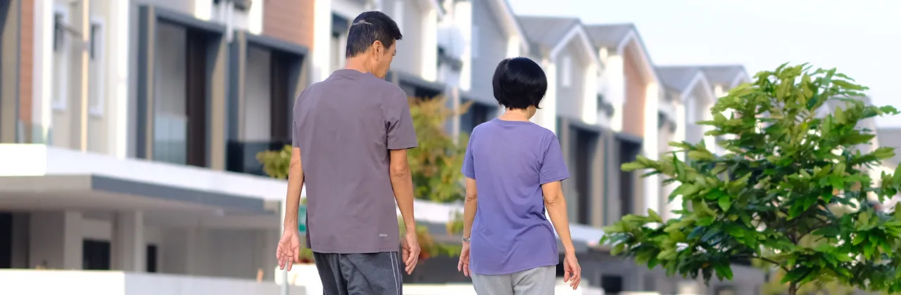 Older Asian couple walking together along a quiet neighborhood street with townhomes in the background