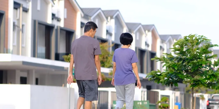 Older Asian couple walking together along a quiet neighborhood street with townhomes in the background