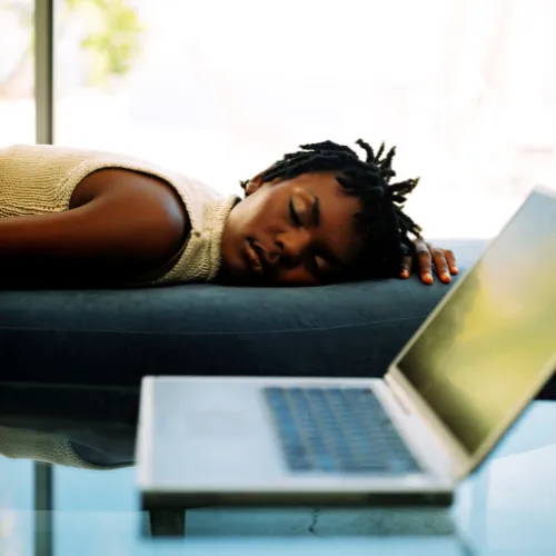 A tired person resting on a couch while still appearing mentally overstimulated and exhausted.