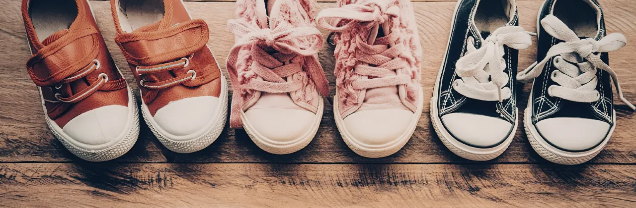 Three pairs of shoes lined up on a wooden floor near a doorway in a lived-in home
