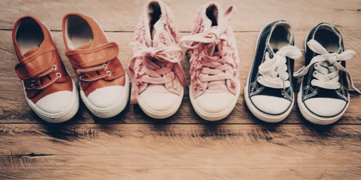Three pairs of shoes lined up on a wooden floor near a doorway in a lived-in home