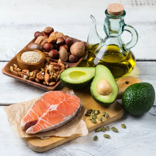 Different food sources of fats including butter, olive oil, nuts, seeds, and avocado arranged for comparison.