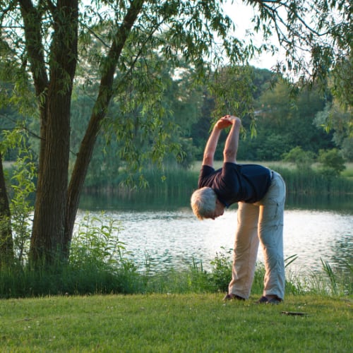 senior man stretching by a lake illustrating movement as a part of better health