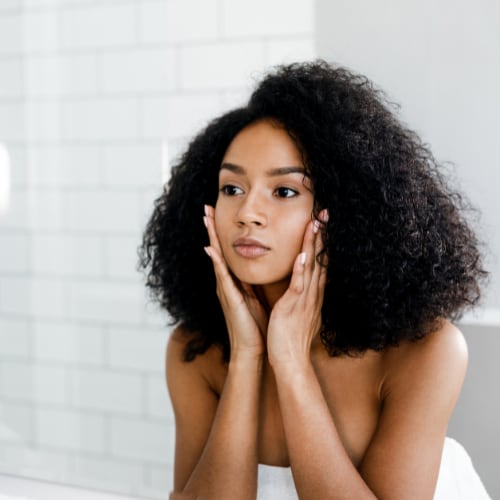 attractive black woman looking at her facial skin in the mirror