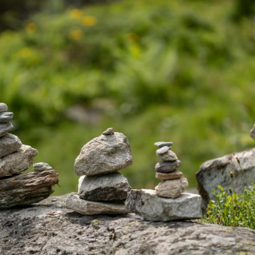 stacked stone cairn with 4 stones on a green nature background depicting the 4 foundations of wellness: eat, move, breathe, think