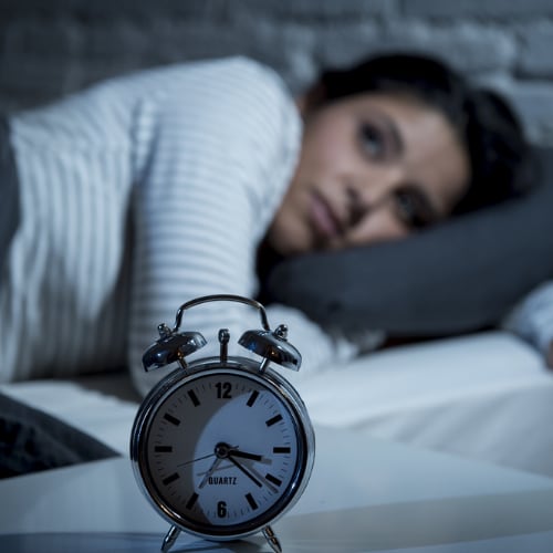 woman lying in bed awake at 3:21 am looking at clock obviously with a lot on her mind