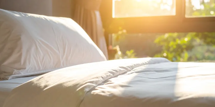 Morning sunlight filtering through bedroom curtains, softly illuminating a bed and pillow in a calm, quiet space