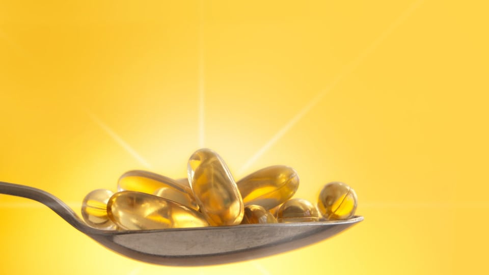 If you are not getting enough Vitamin D naturally from sunshine, consider augmenting your diet with NuMedica D3-5000. a spoonful of Vitamin D softgels with bright sun in the background depicting how sunlight is a good way to get Vitamin D naturally