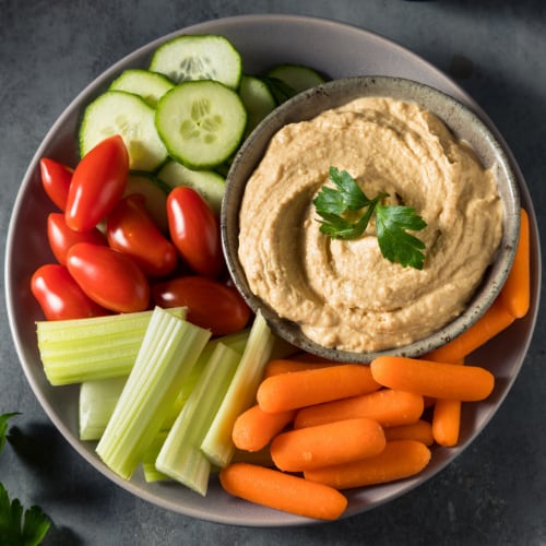 assorted vegetablds including cucumbers, tomotatoes, celery, and carrots with hummus served as a snack tray