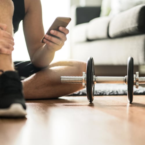 workout dumbbell on living room floor with man looking at fitness app on phone