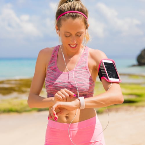 younger woman outside exercising looking at her watch which is monitoring biomarkers