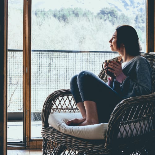 a woman sitting at home comfortably in her chair with a healthy drink staring out the window relaxing