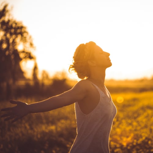 woman outside in a field full of sunshine breathing deeply