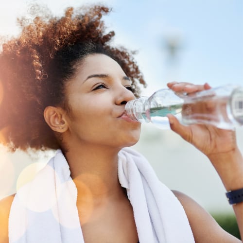black woman drinking water from a bottle after working out 