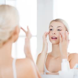 woman examining her facial skin in the bathroom mirror
