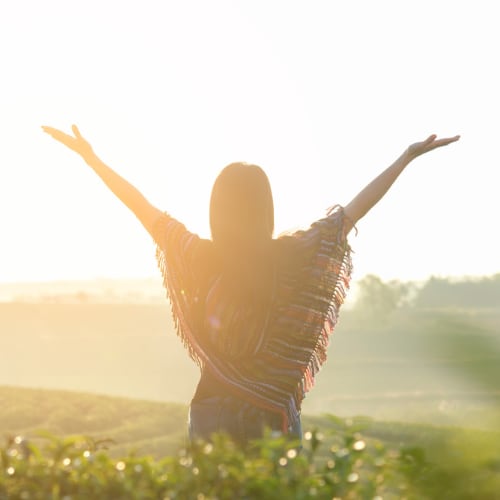 woman standing in field with arms raised taking in the beauty of nature