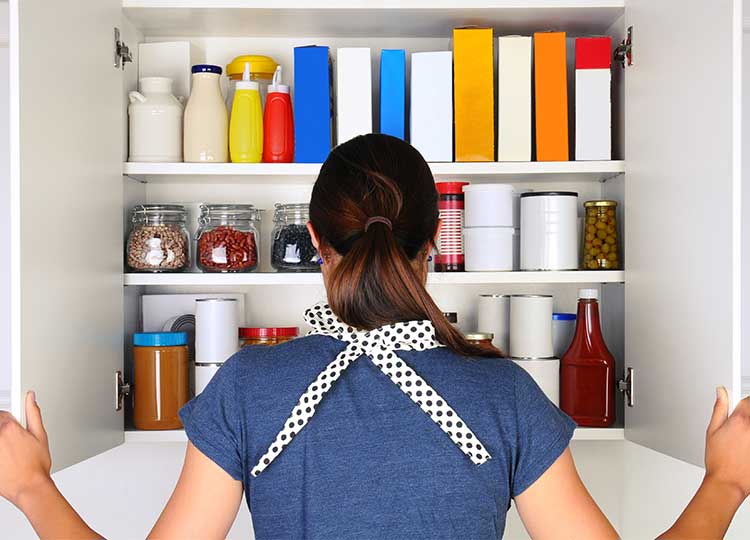 Young Caucasian Woman Looking into Well Stocked Cupboard