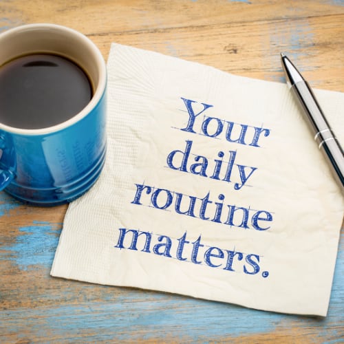 the words your daily routine matters on a napkin with a cup of coffee and pen